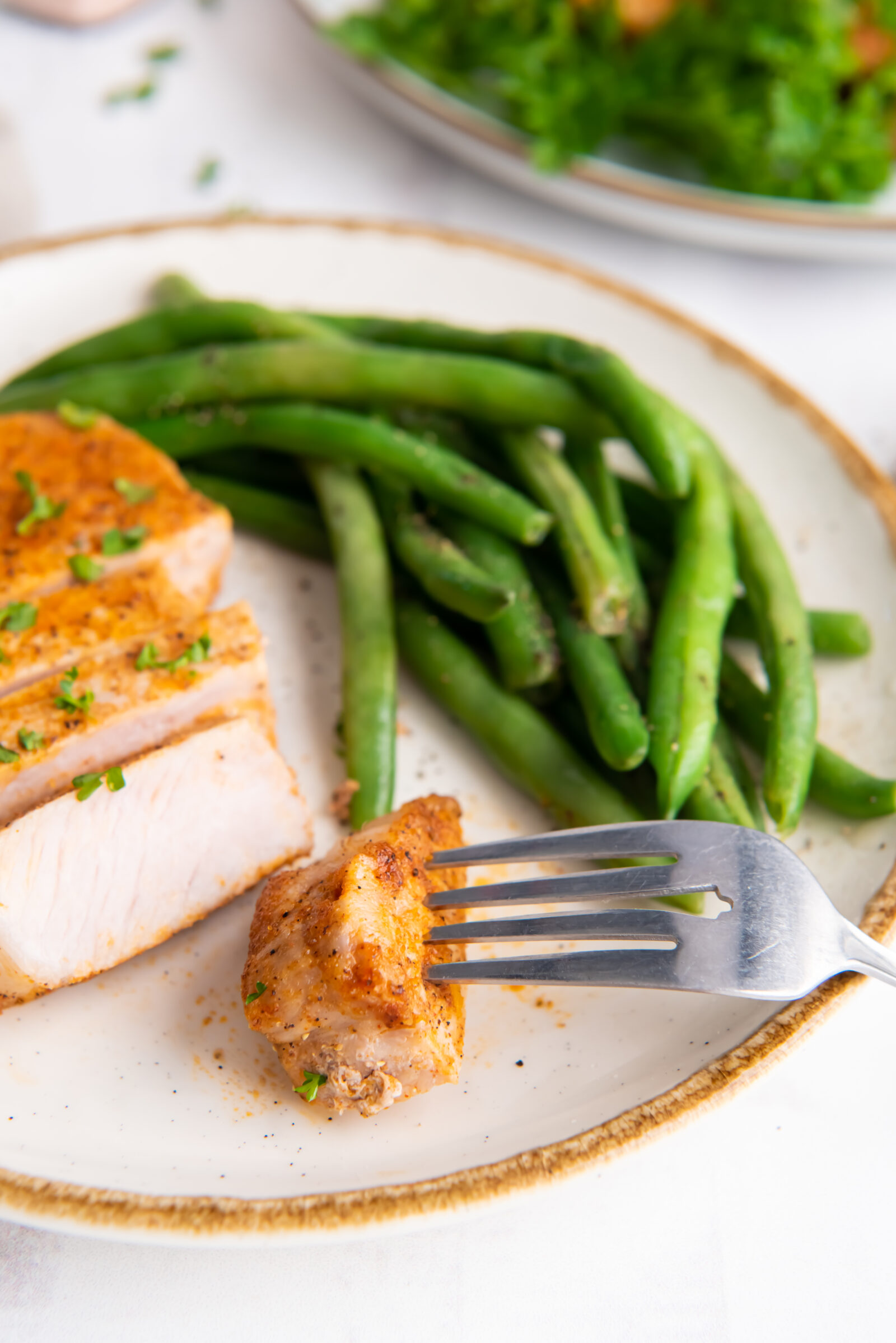 A sliced air fryer pork chop with green beans on a white speckled plate