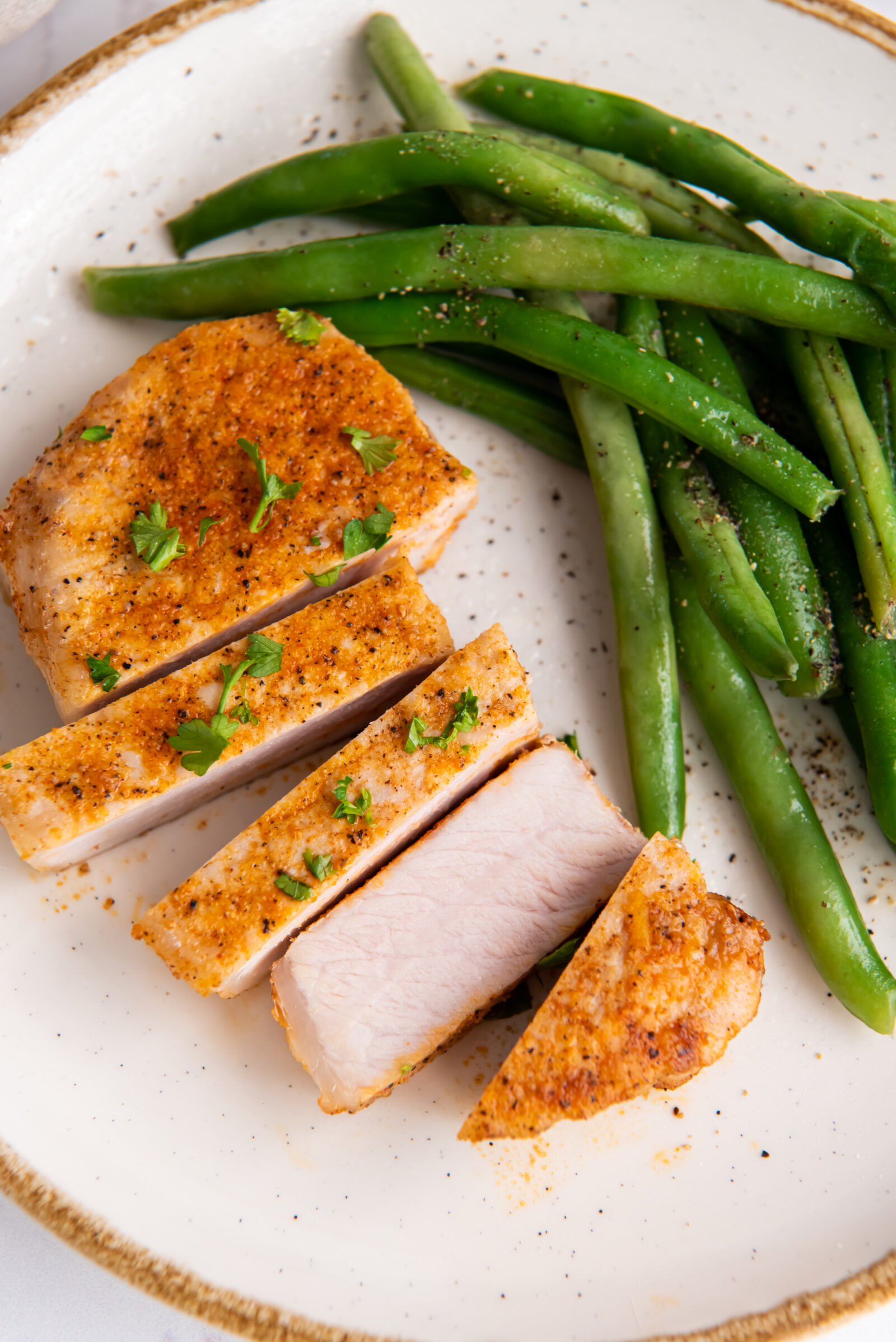 Sliced air fryer boneless pork chop with green beans on a white plate