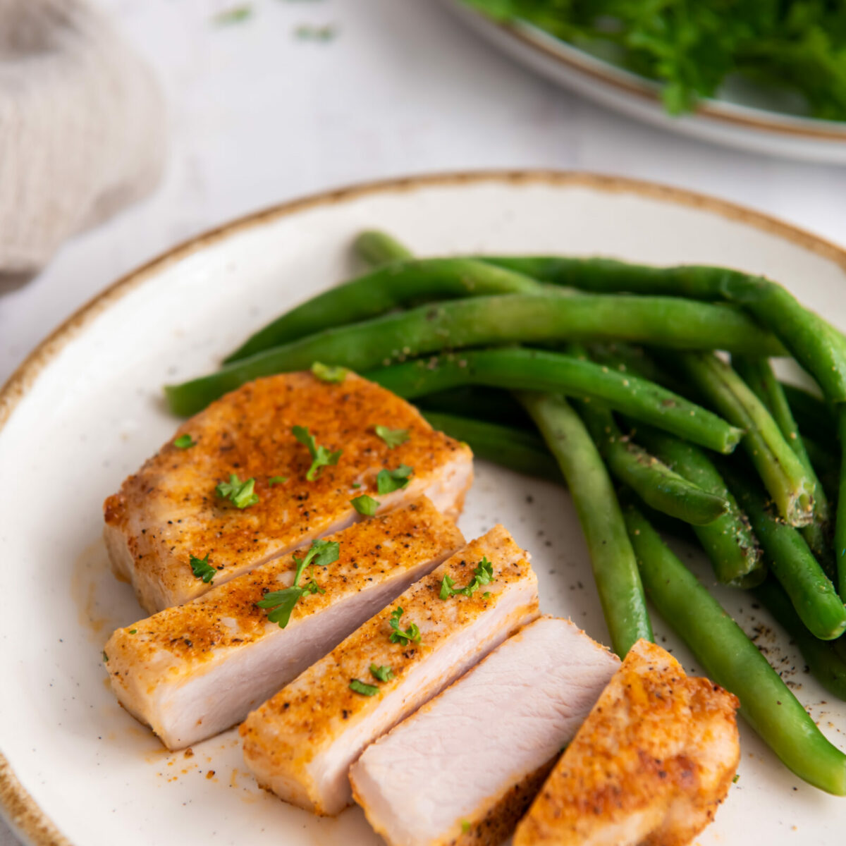 Sliced air fryer boneless pork chop with green beans on a white plate