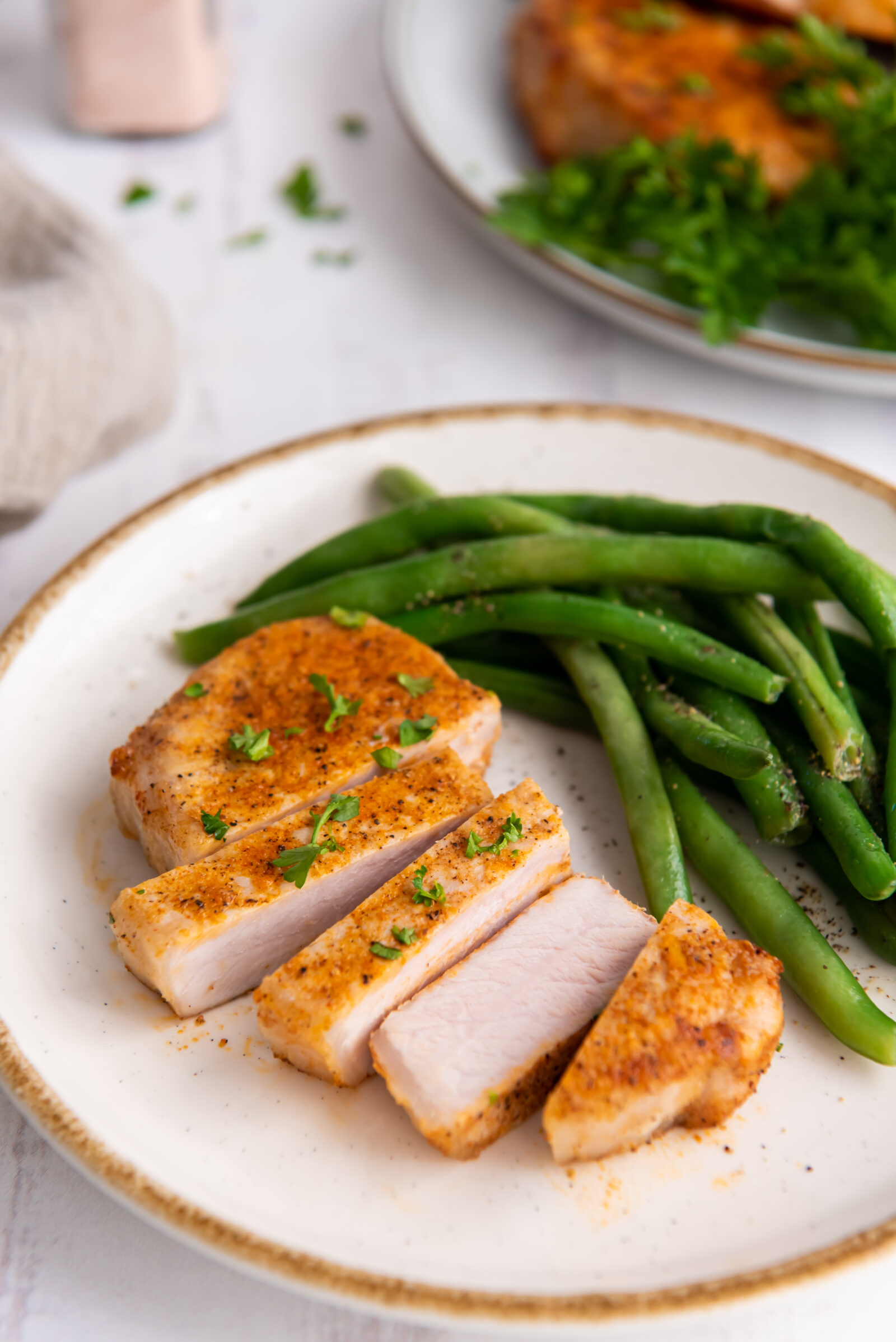 Sliced air fryer boneless pork chop with green beans on a white plate