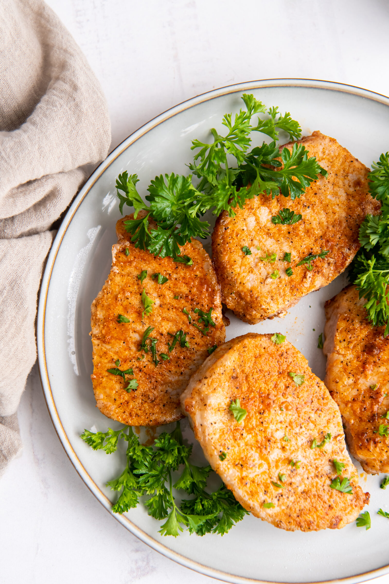 Overhead view of four air fryer pork chops garnished with fresh parsley