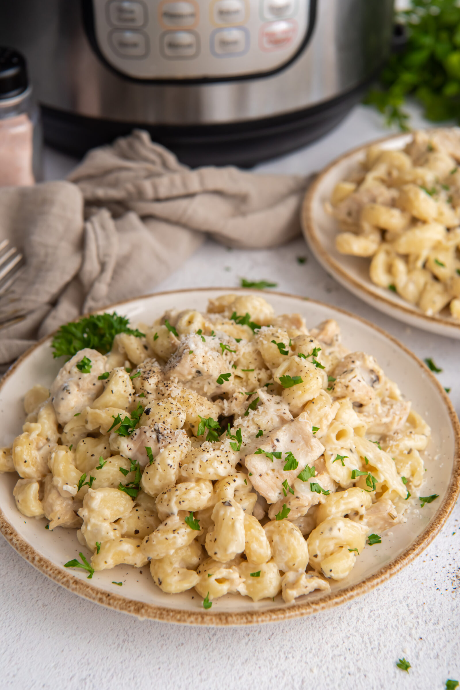 Two plates of Instant Pot creamy chicken pasta in white sauce, with Instant Pot in background. 