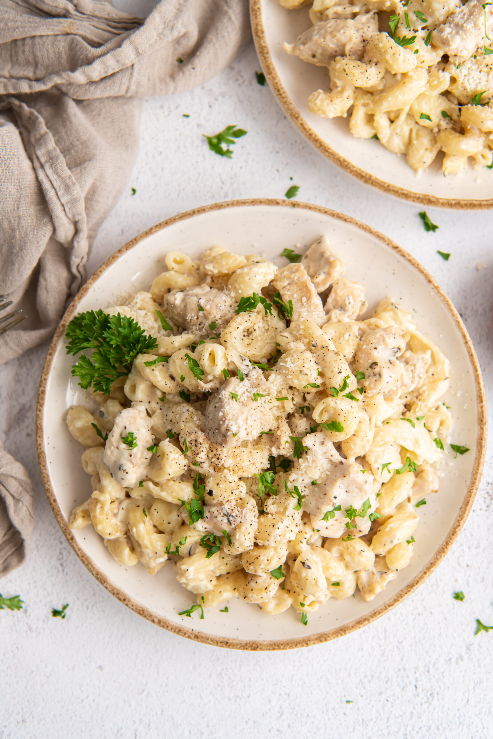 Overhead view of two plates of creamy garlic chicken pasta, garnished with fresh parsley. 