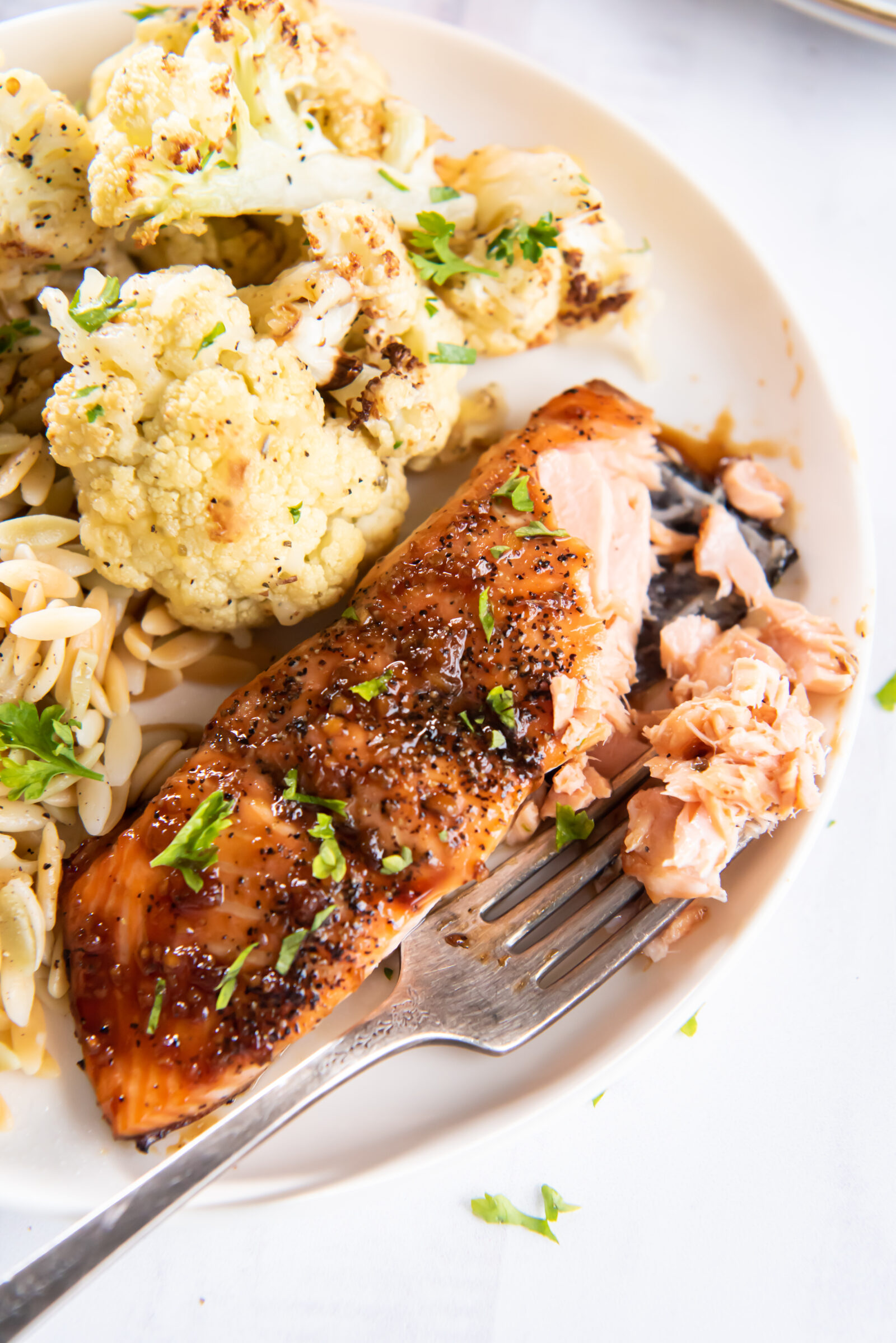 Flaked maple soy glazed salmon, orzo, and cauliflower on a white plate. 