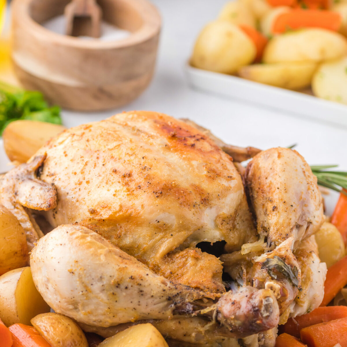 A whole chicken with potatoes and carrots on a serving platter. 
