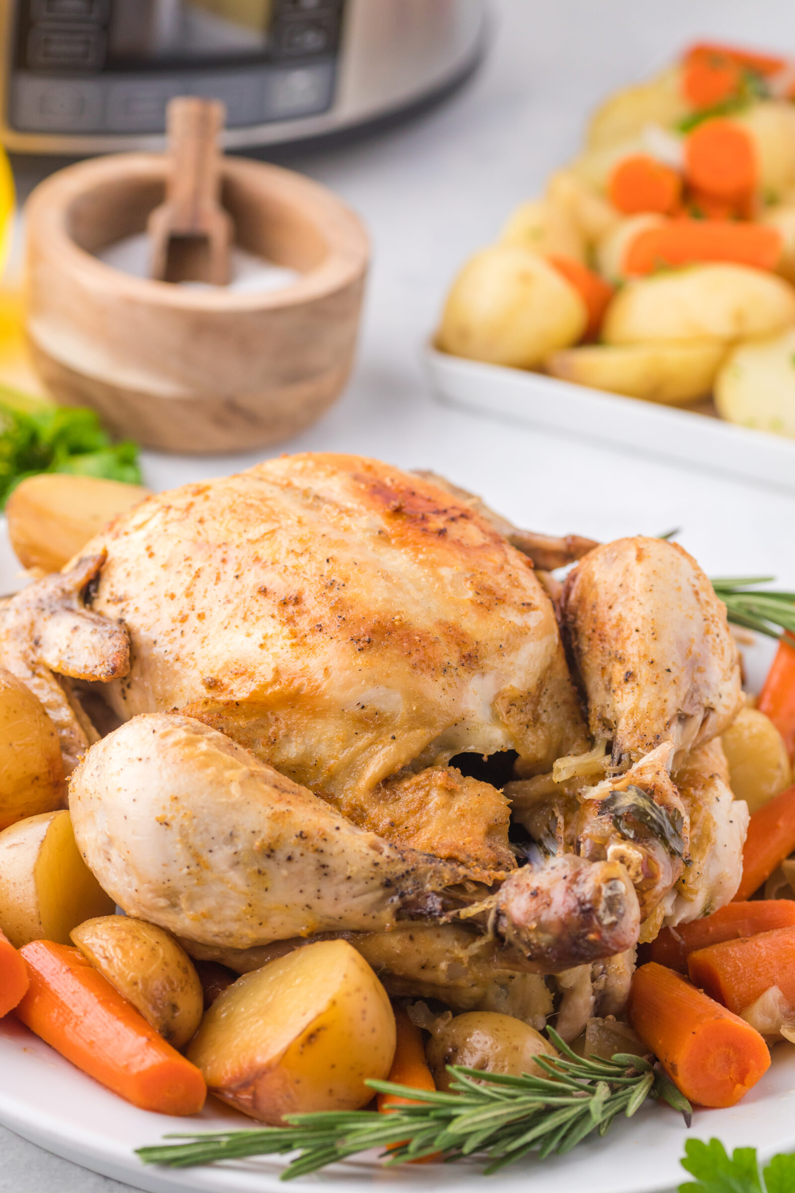 A whole chicken with potatoes and carrots on a serving platter. 