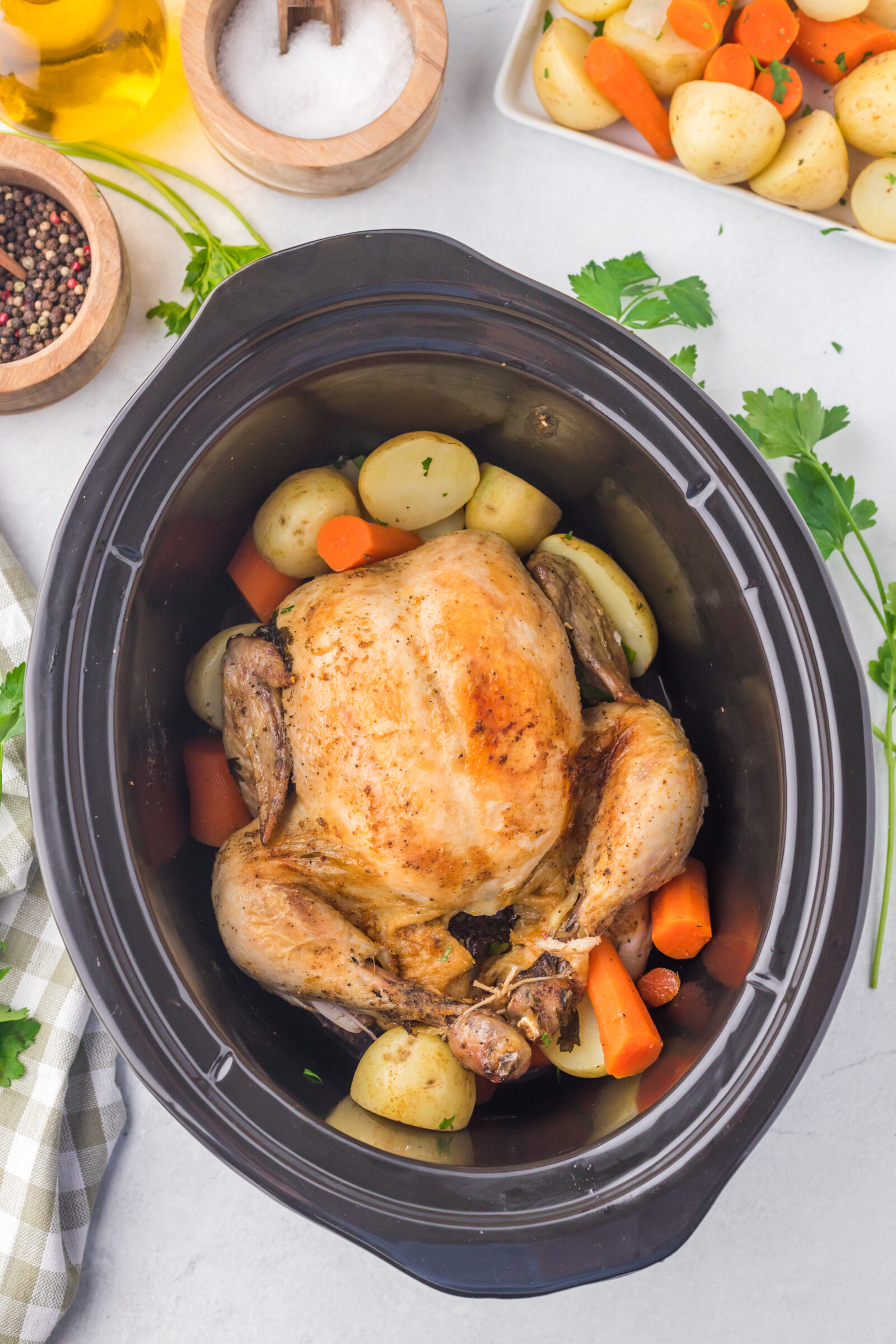 Overhead view of a slow cooker whole chicken with potatoes and carrots. 