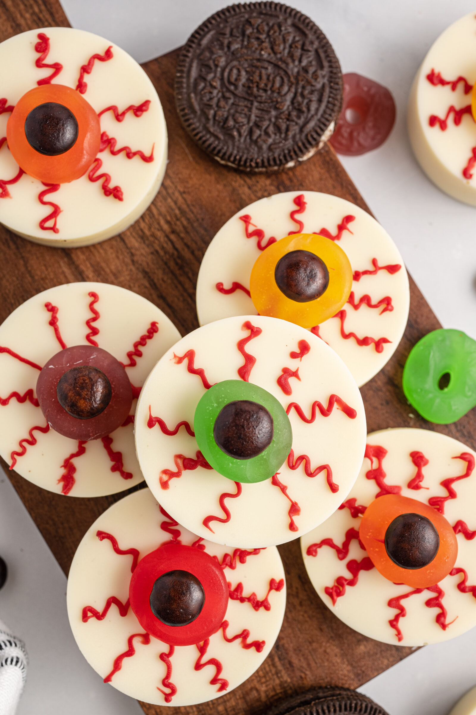 An overhead view of Halloween chocolate covered Oreo eyeballs piled on a wooden cutting board. 