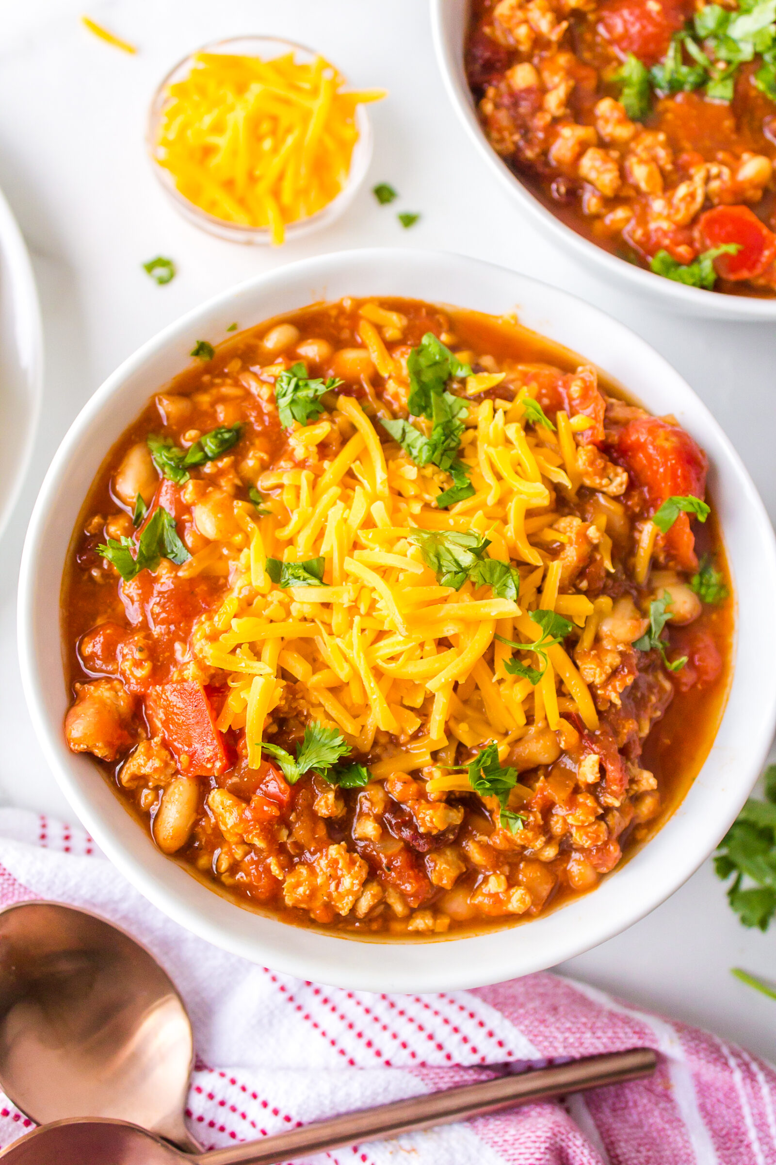 An overhead view of a bowl of ground turkey and white bean chili garnished with shredded cheese and chives. 