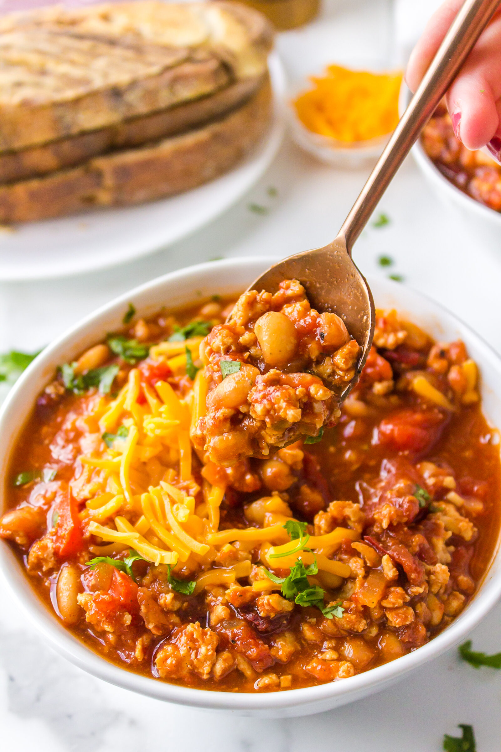 A bowl of white bean turkey chili, topped with shredded cheese and chives. 