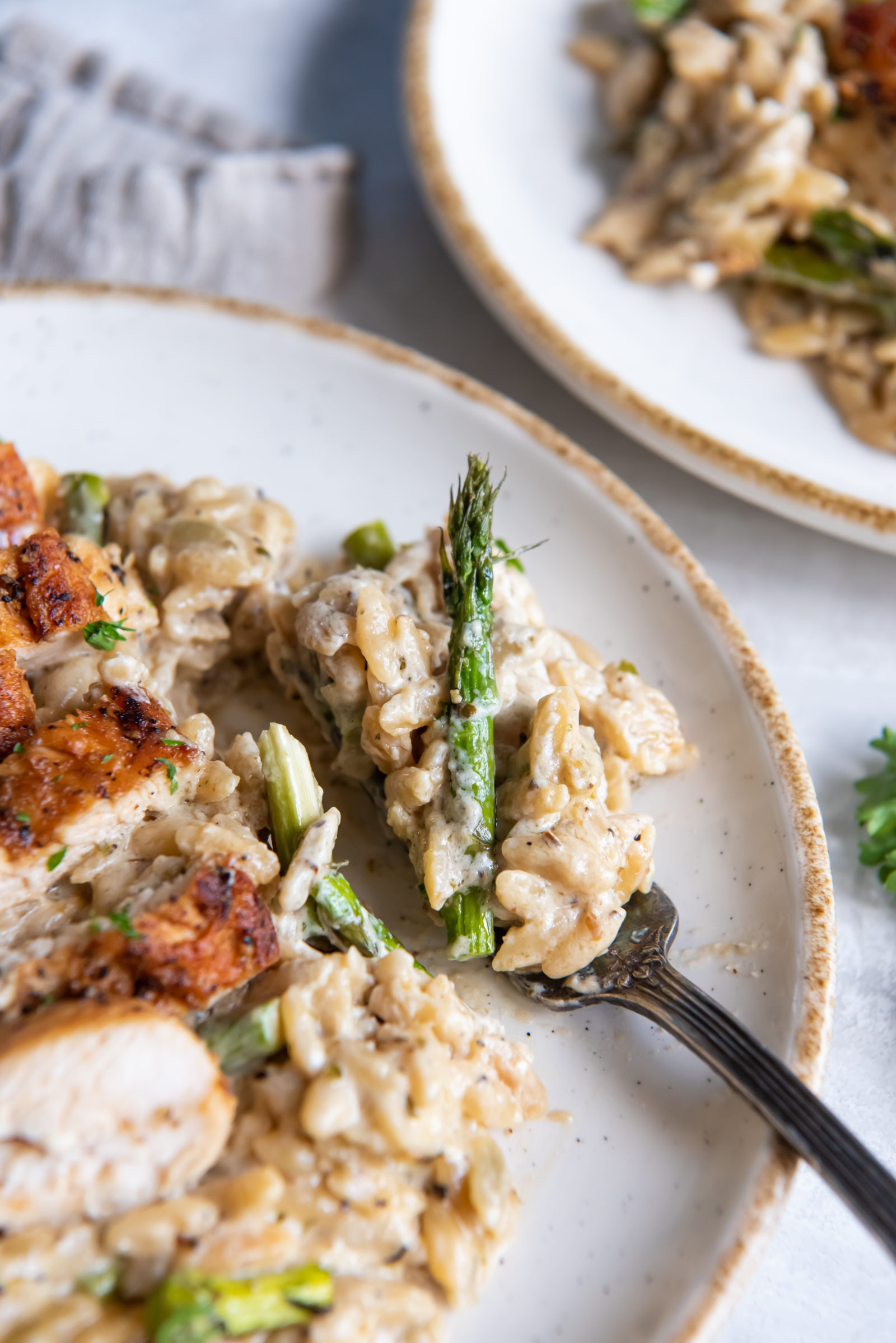 A close up view of orzo with asparagus and chicken on white plates. 