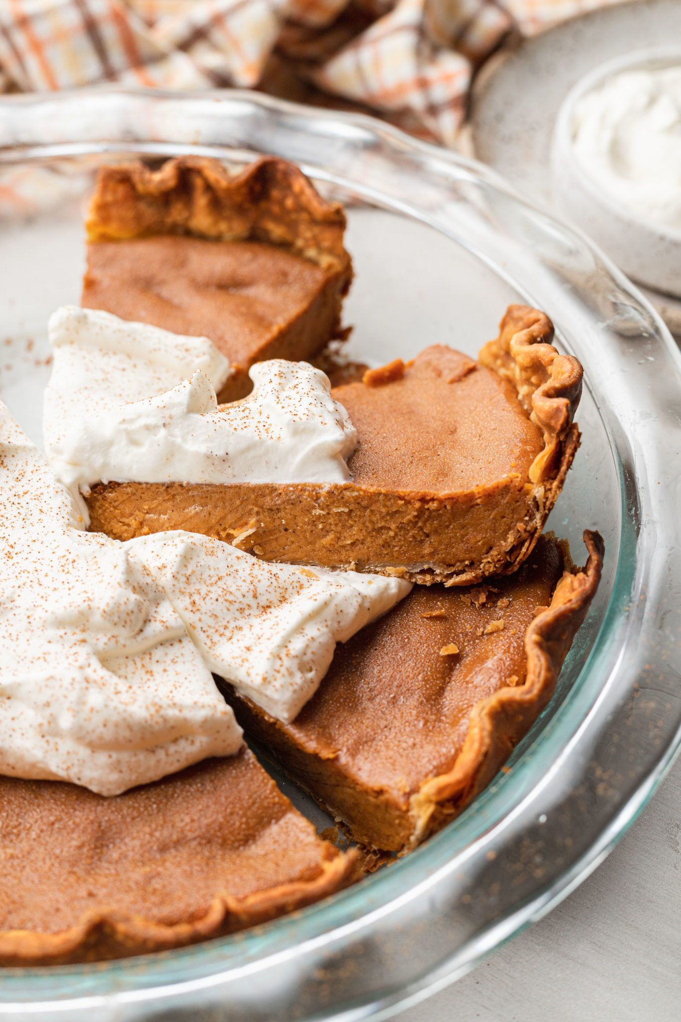 slice of eggless pumpkin pie on a transparent plate with whipped cream on top