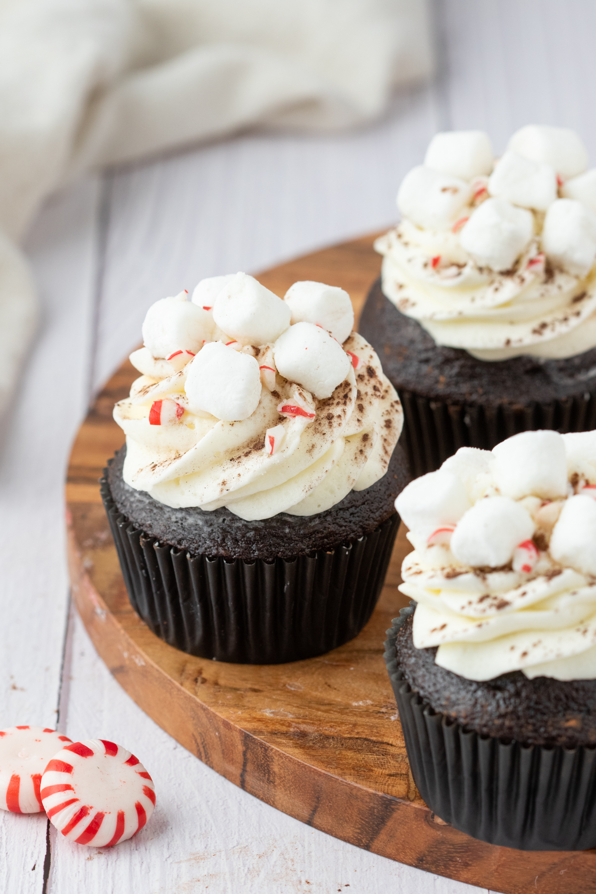 Marshmallow frosted hot cocoa cupcakes on a wooden platter. 
