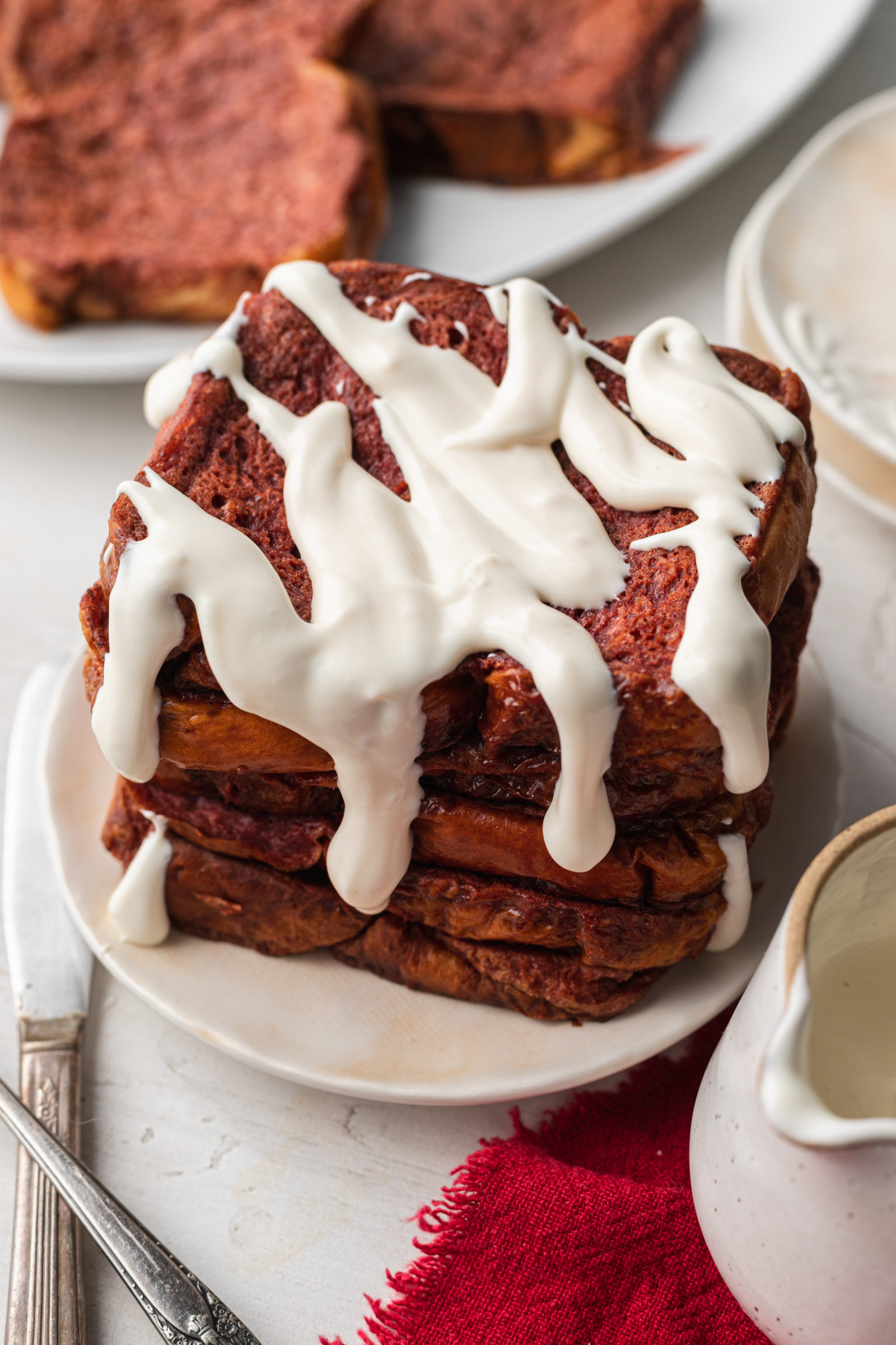 A stack of red velvet french toast topped with cream cheese drizzle. 