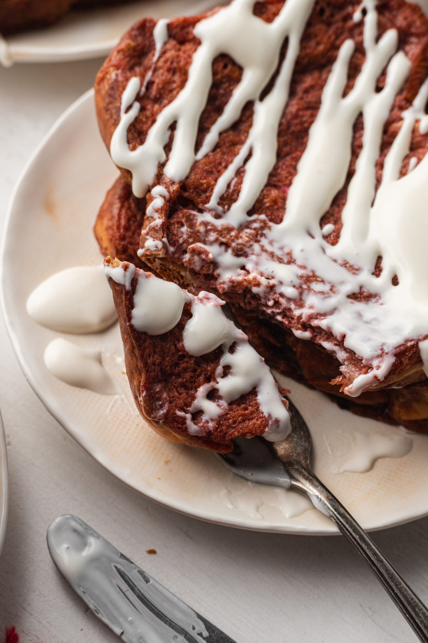A slice of red velvet french toast topped with cream cheese drizzle.