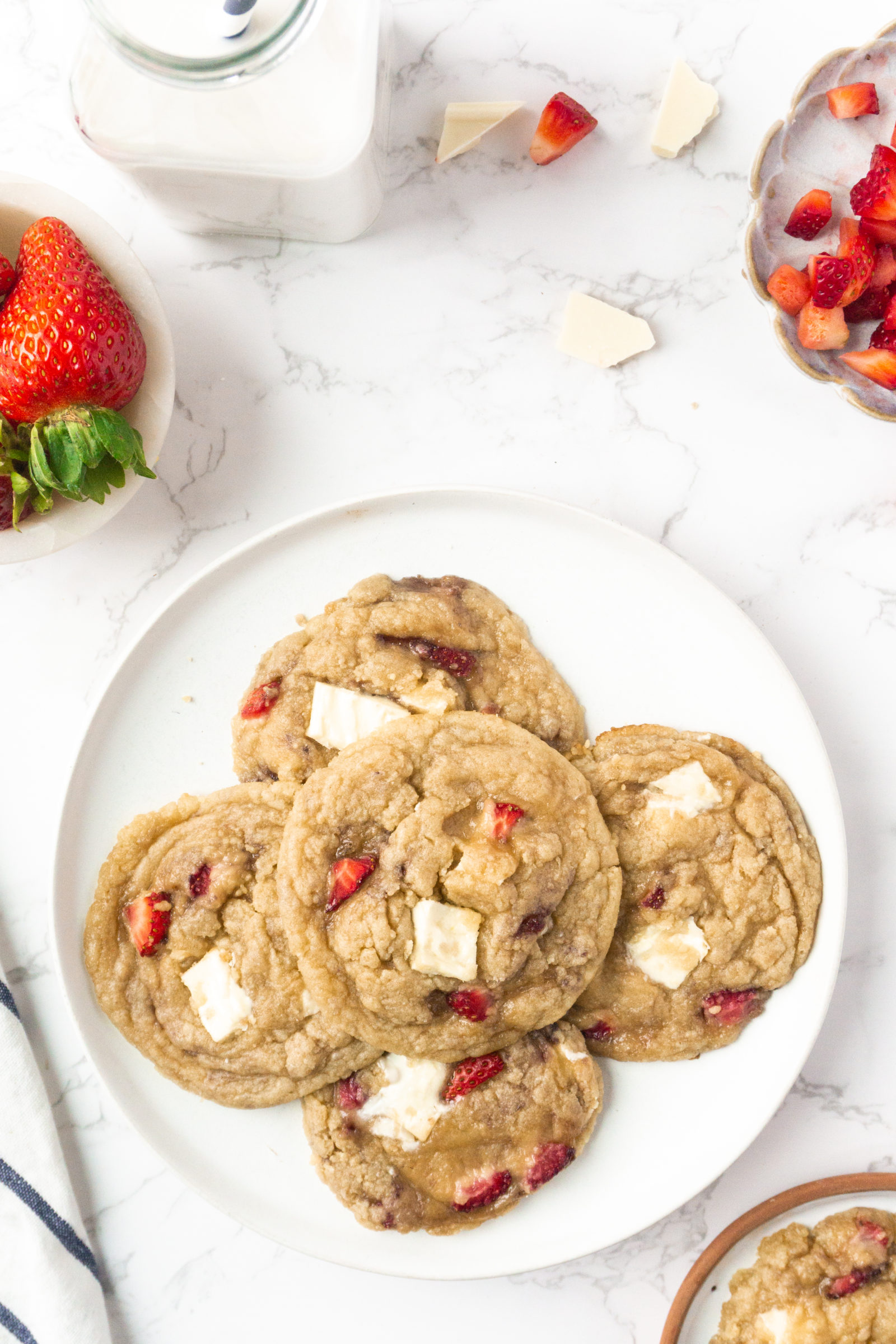 An overhead view of strawberry white chocolate cookies on a white plate, next to a dish of berries. 