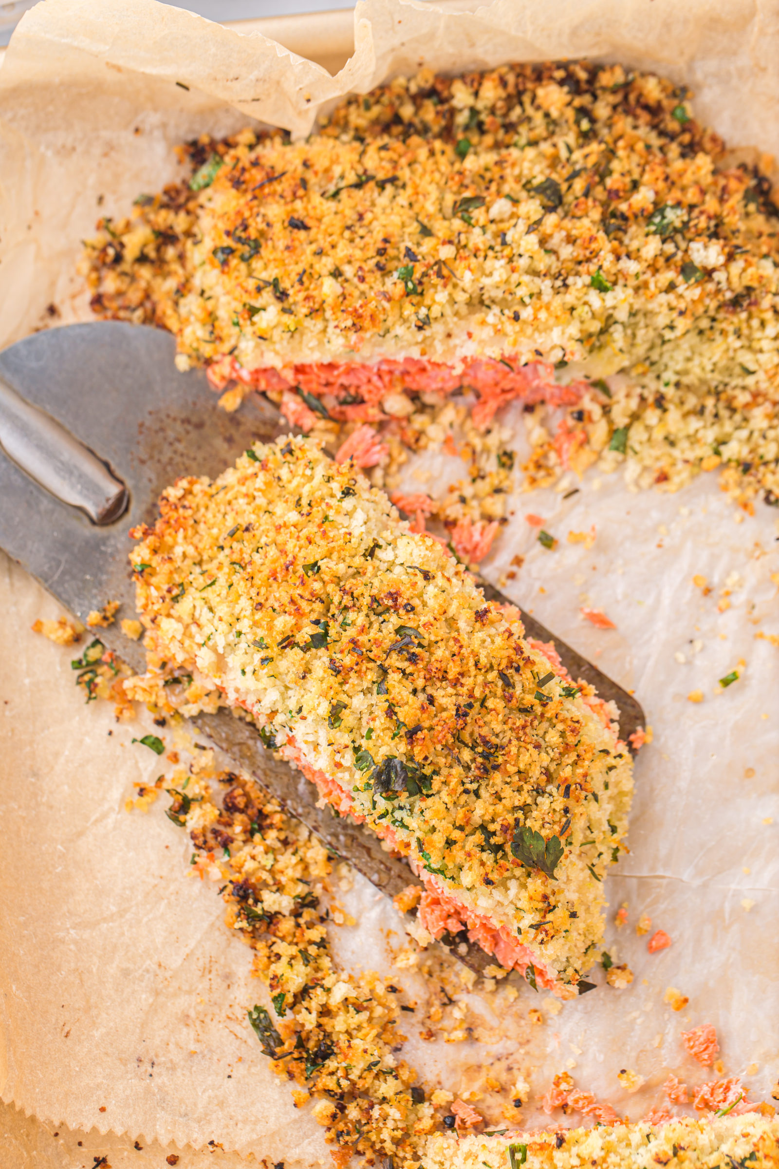 An overhead view of an herb and panko crusted salmon filet on a parchment lined baking sheet.