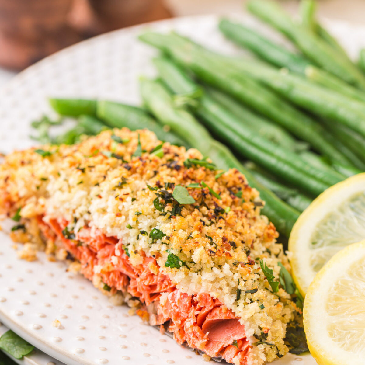 An herb crusted salmon filet on a plate with lemon slices and green beans.