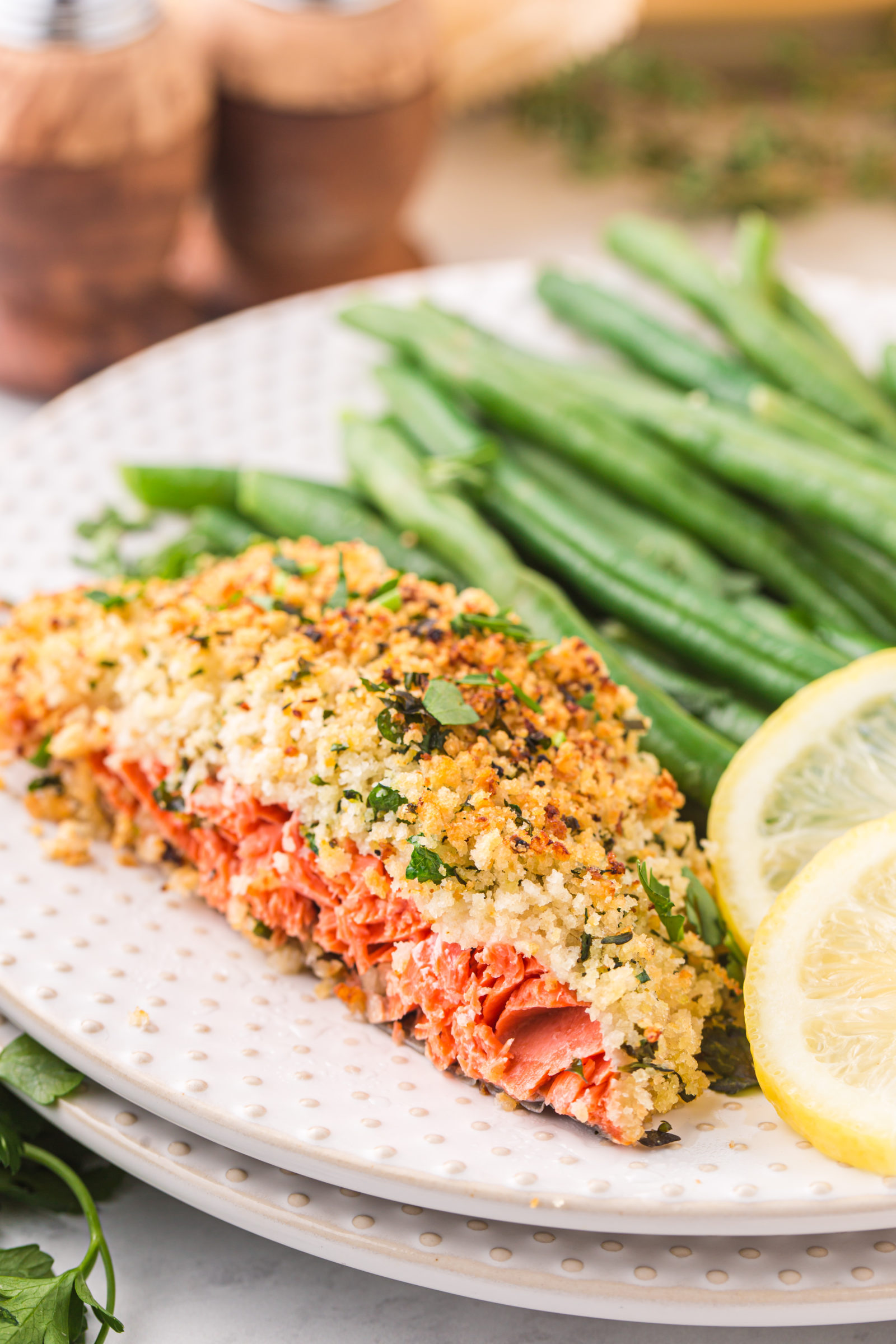 An herb crusted salmon filet on a plate with lemon slices and green beans. 