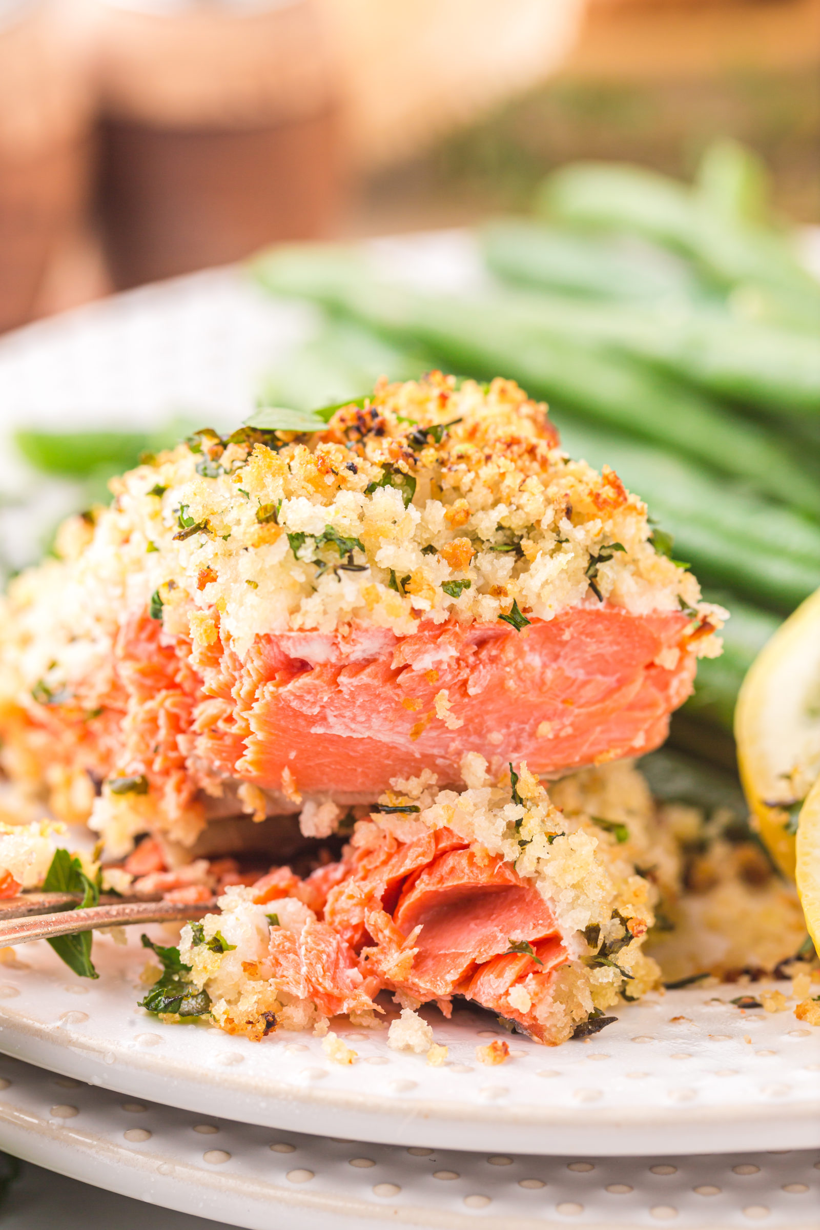 An herb crusted filet of salmon being lifted with a fork off of a white plate. 