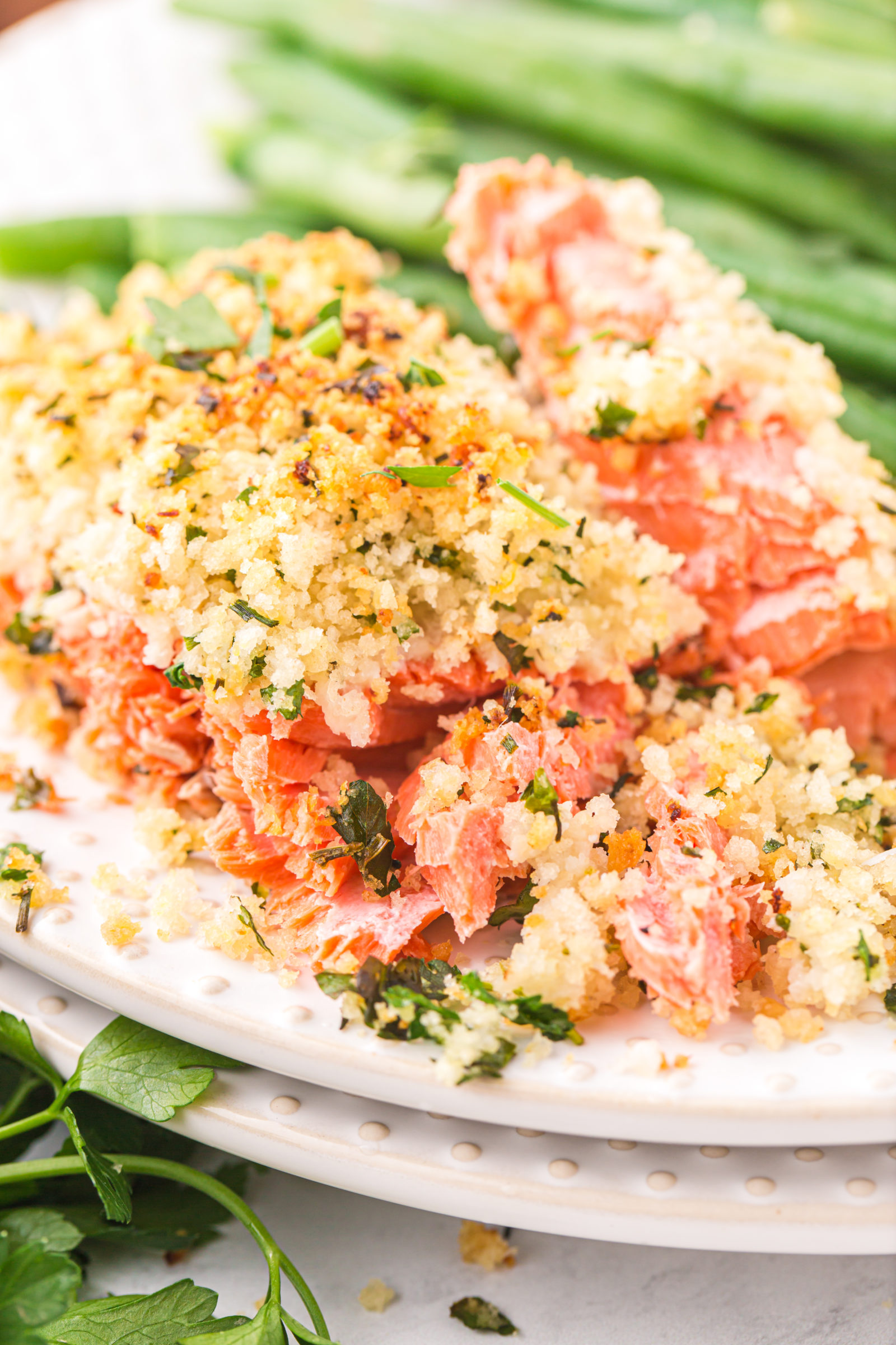 A serving of salmon with an herb crust on a white plate with green beans. 