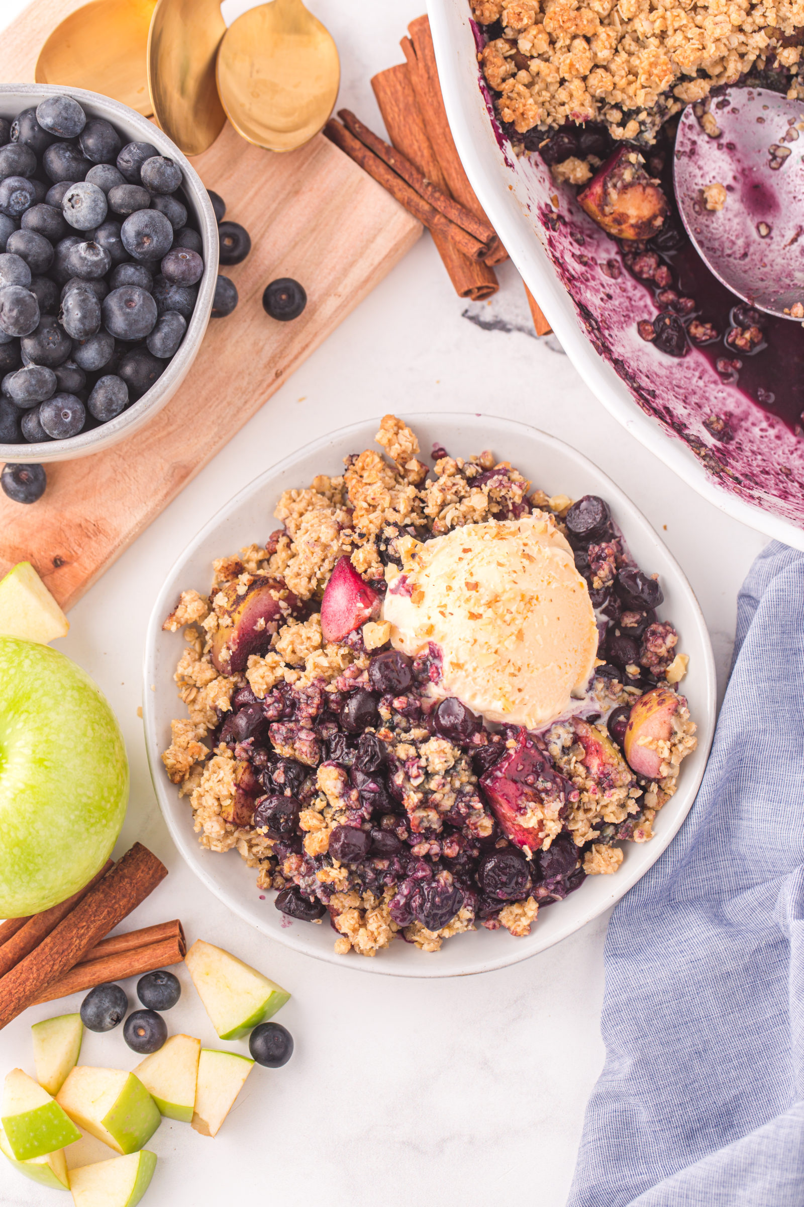 An overhead view of a portion of berry apple crumble topped with vanilla ice cream. 