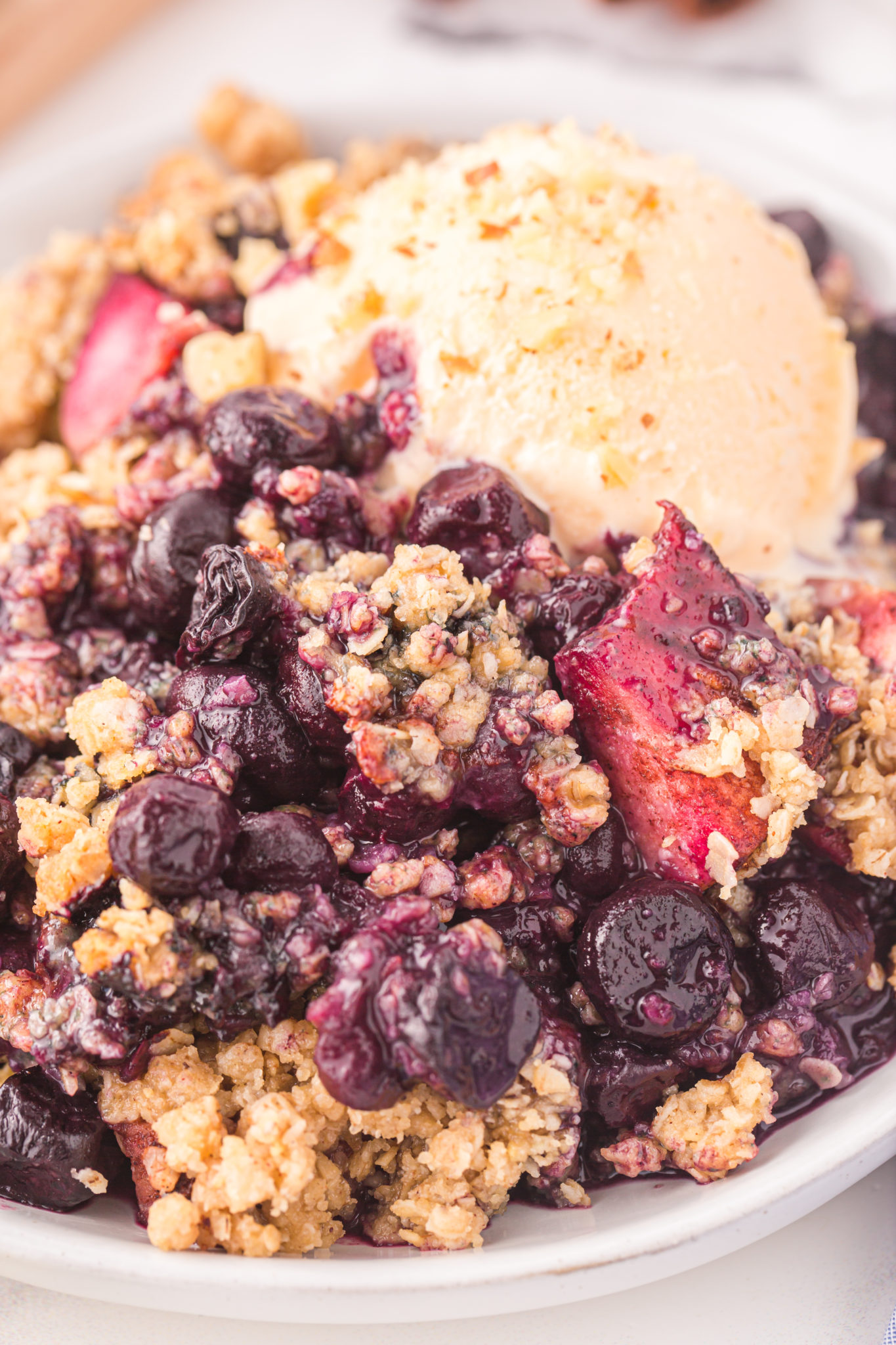 A serving of apple blueberry crumble, featuring a crumble topping with oats and vanilla ice cream.