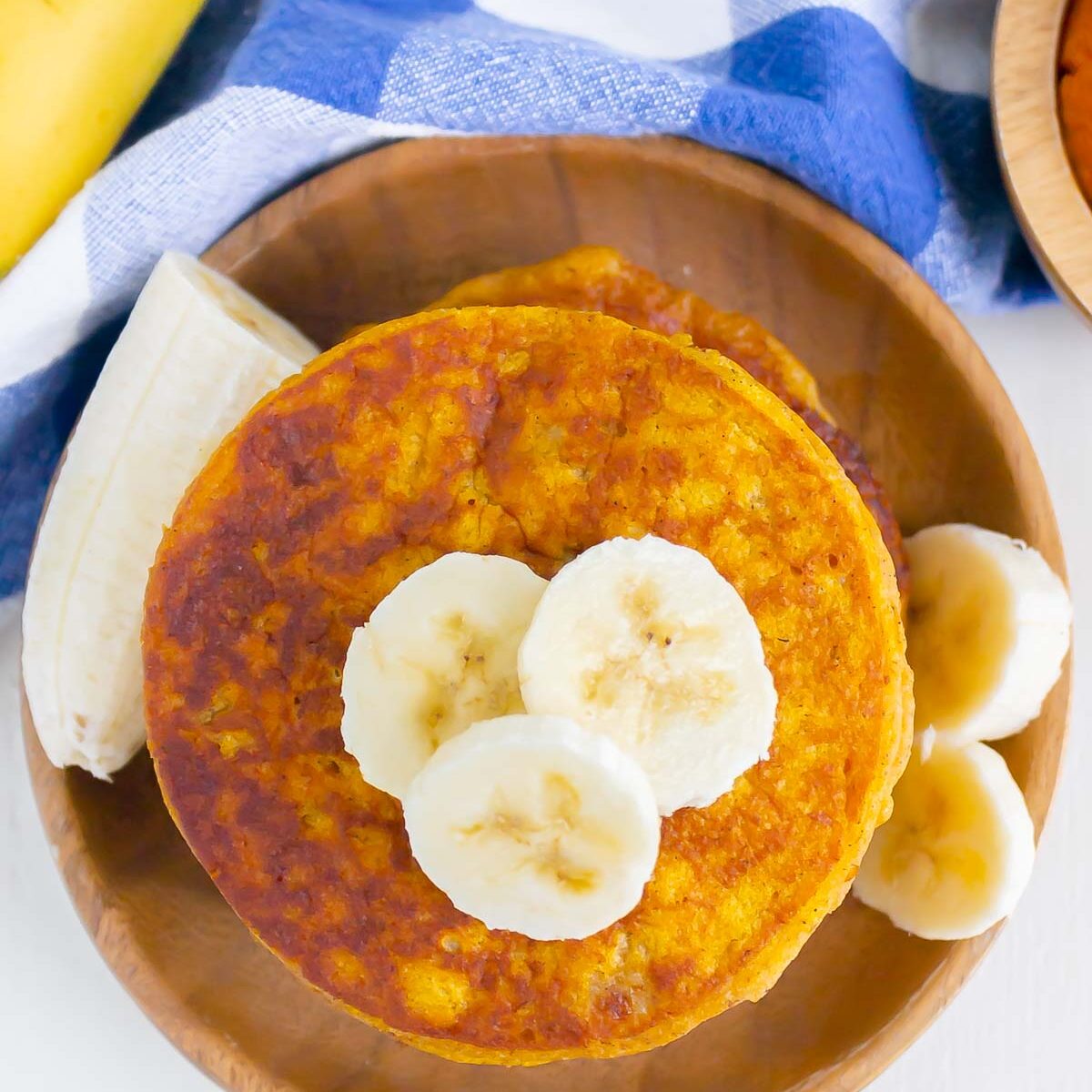 overview of banana pumpkin pancakes, drizzled with maple syrup and topped with banana slices, on a wooden plate