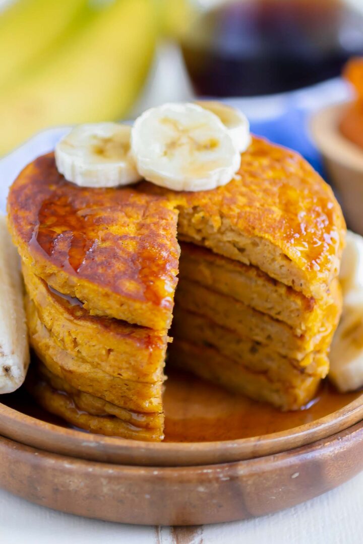 stack of pancakes with a slice cut out on a wooden plate