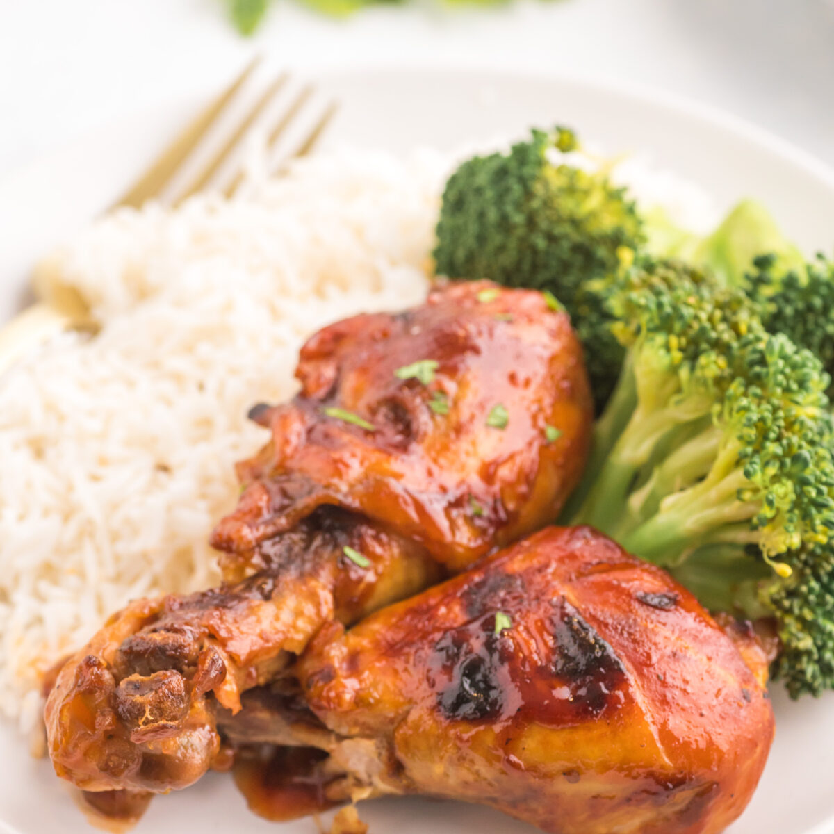 chicken legs on a white plate with rice and broccoli
