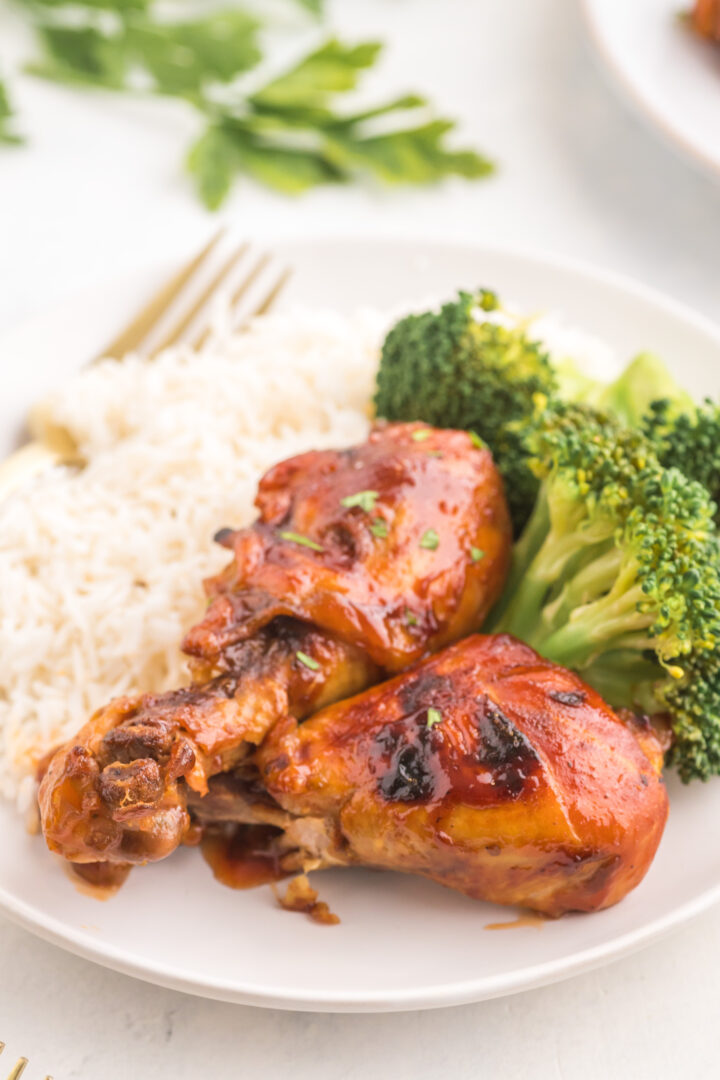 chicken legs on a white plate with rice and broccoli