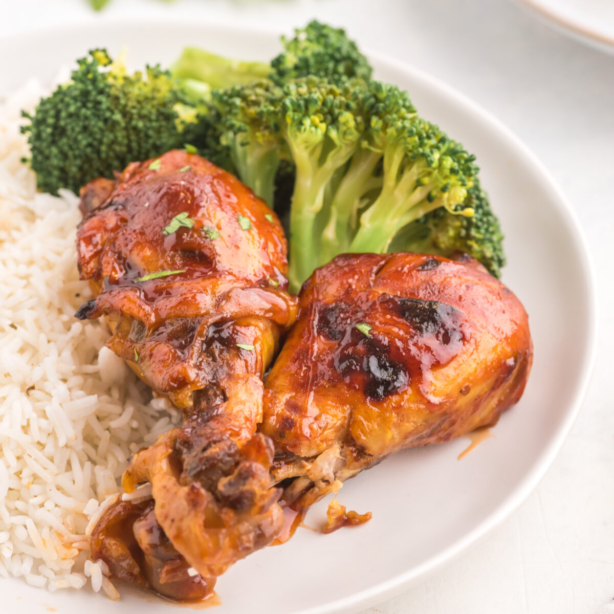 chicken legs on a white plate with rice and broccoli