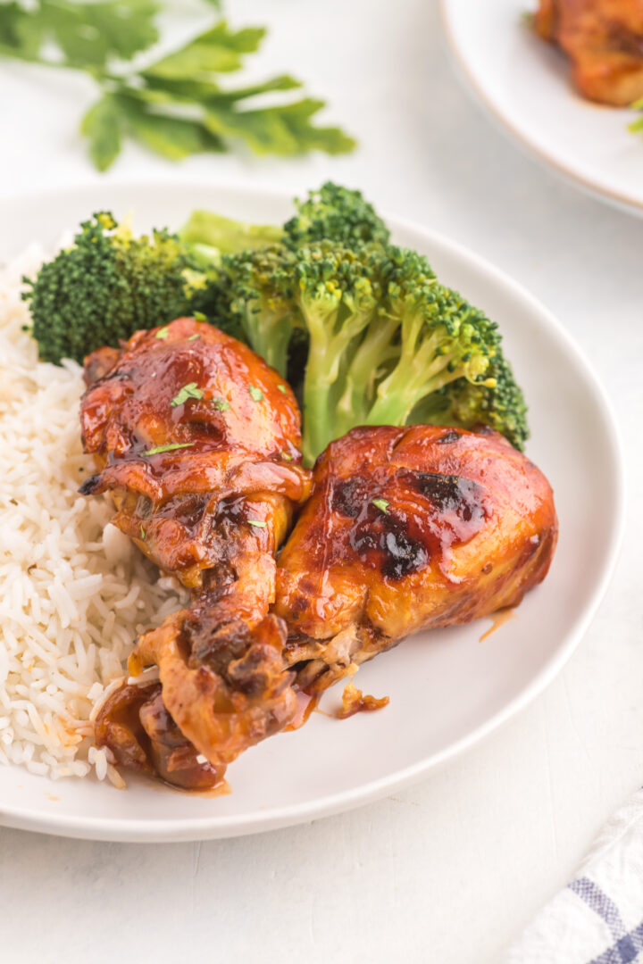 chicken legs on a white plate with rice and broccoli