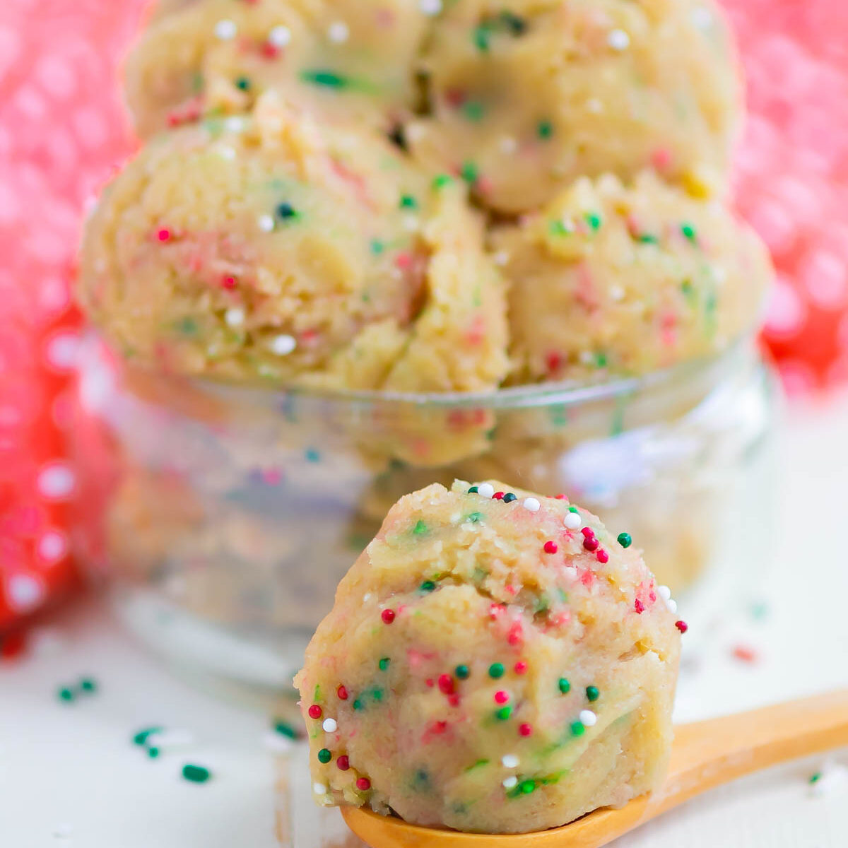 cookie dough in a mini glass jar with a wooden spoon in front with a scoop of dough