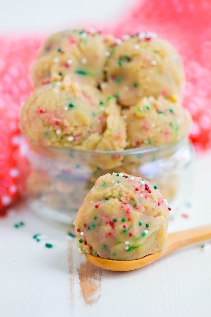 cookie dough in a mini glass jar with a wooden spoon in front with a scoop of dough