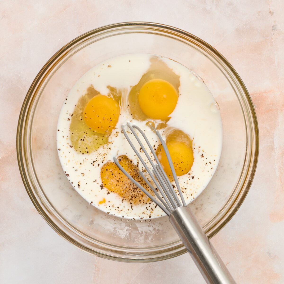 eggs and milk in a glass bowl with a whisk