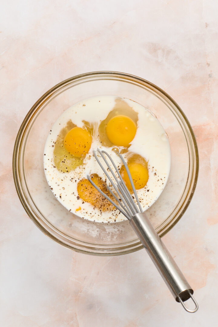 eggs and milk in a glass bowl with a whisk