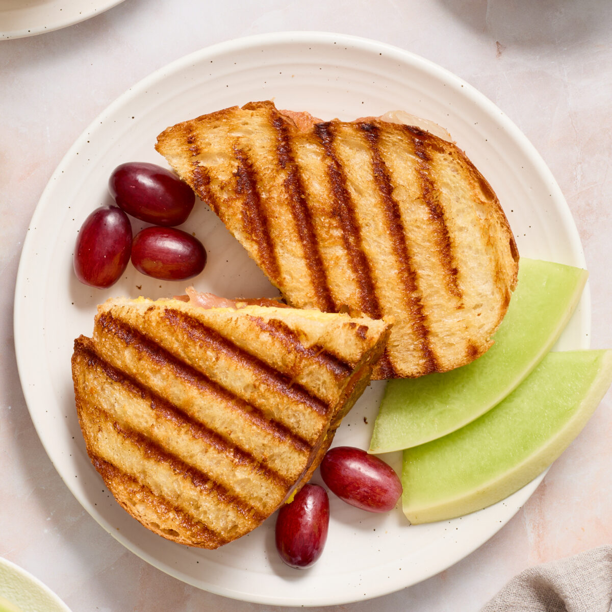 panini on a white plate with red grapes and green melon