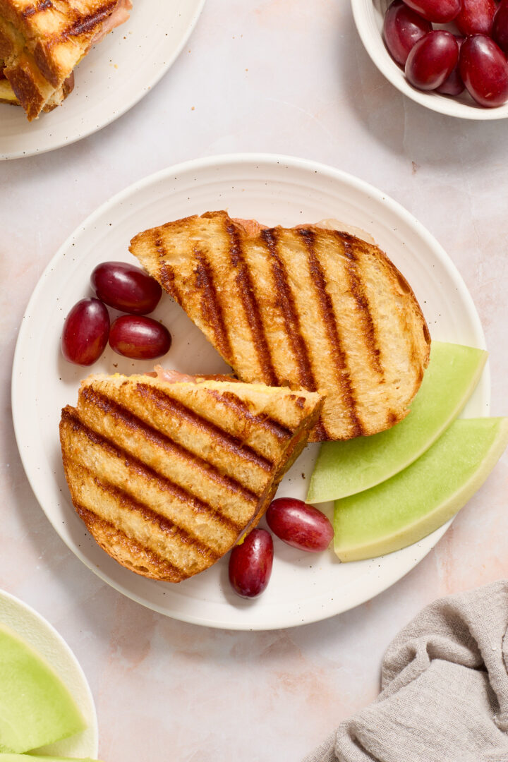 panini on a white plate with red grapes and green melon