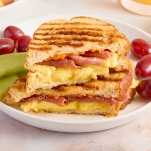 panini on a white plate with red grapes and green melon