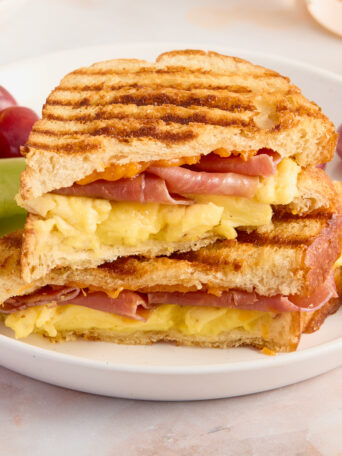 panini on a white plate with red grapes and green melon