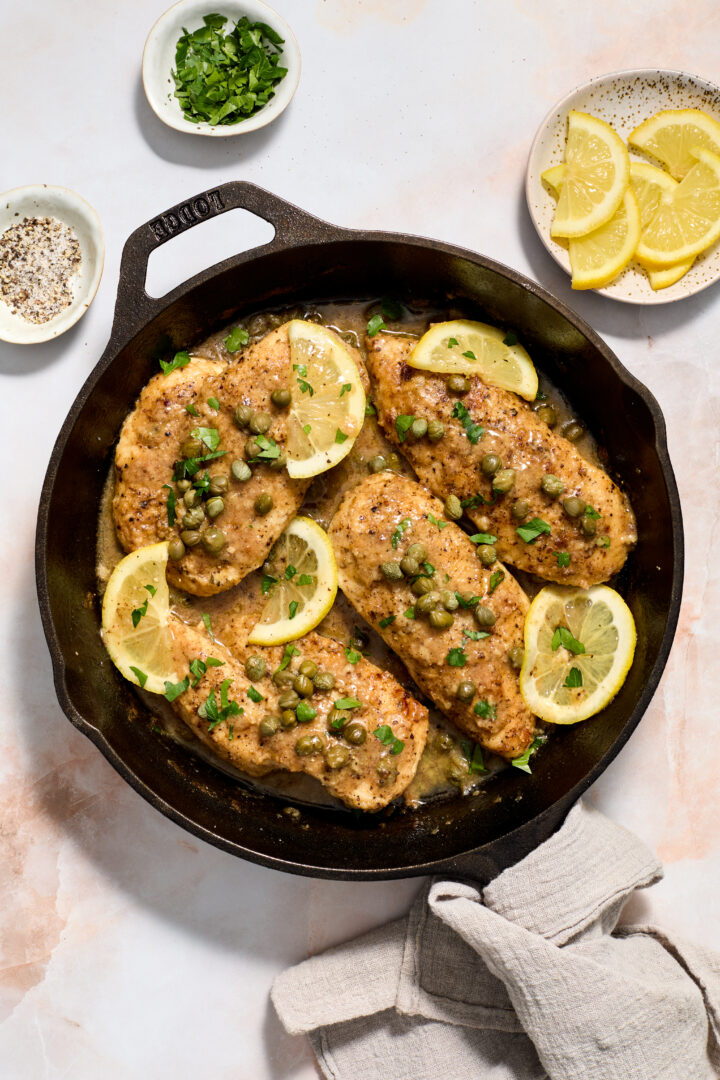 chicken piccata in a black skillet with lemon slices