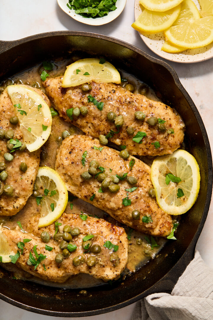 chicken piccata in a black skillet with lemon slices