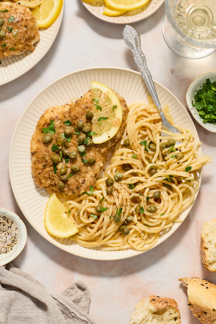 chicken piccata on a white plate with noodles and lemon slices