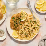 chicken piccata on white plate with noodles and lemon slices