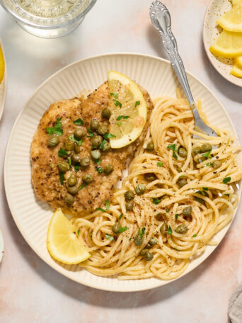 chicken piccata on white plate with noodles and lemon slices