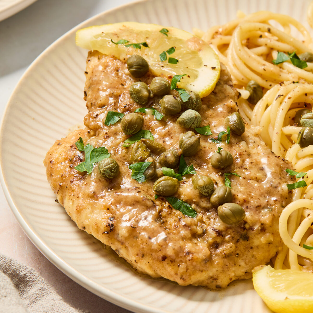 chicken piccata on a white plate with noodles and lemon slices