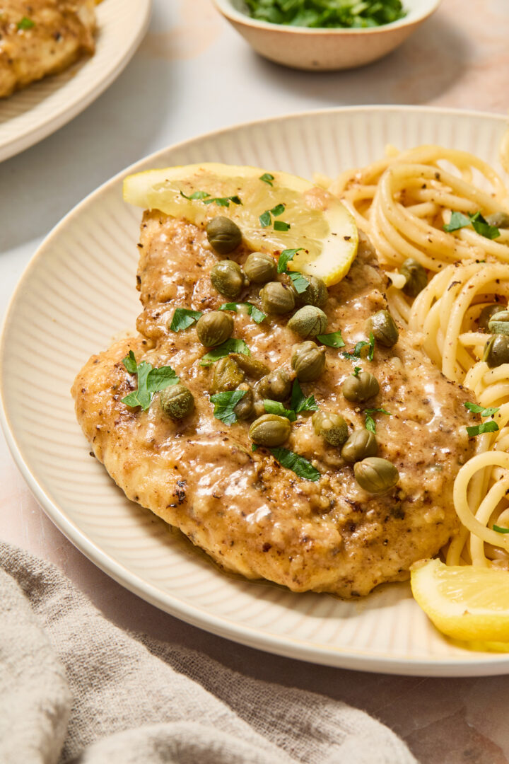 chicken piccata on a white plate with noodles and lemon slices