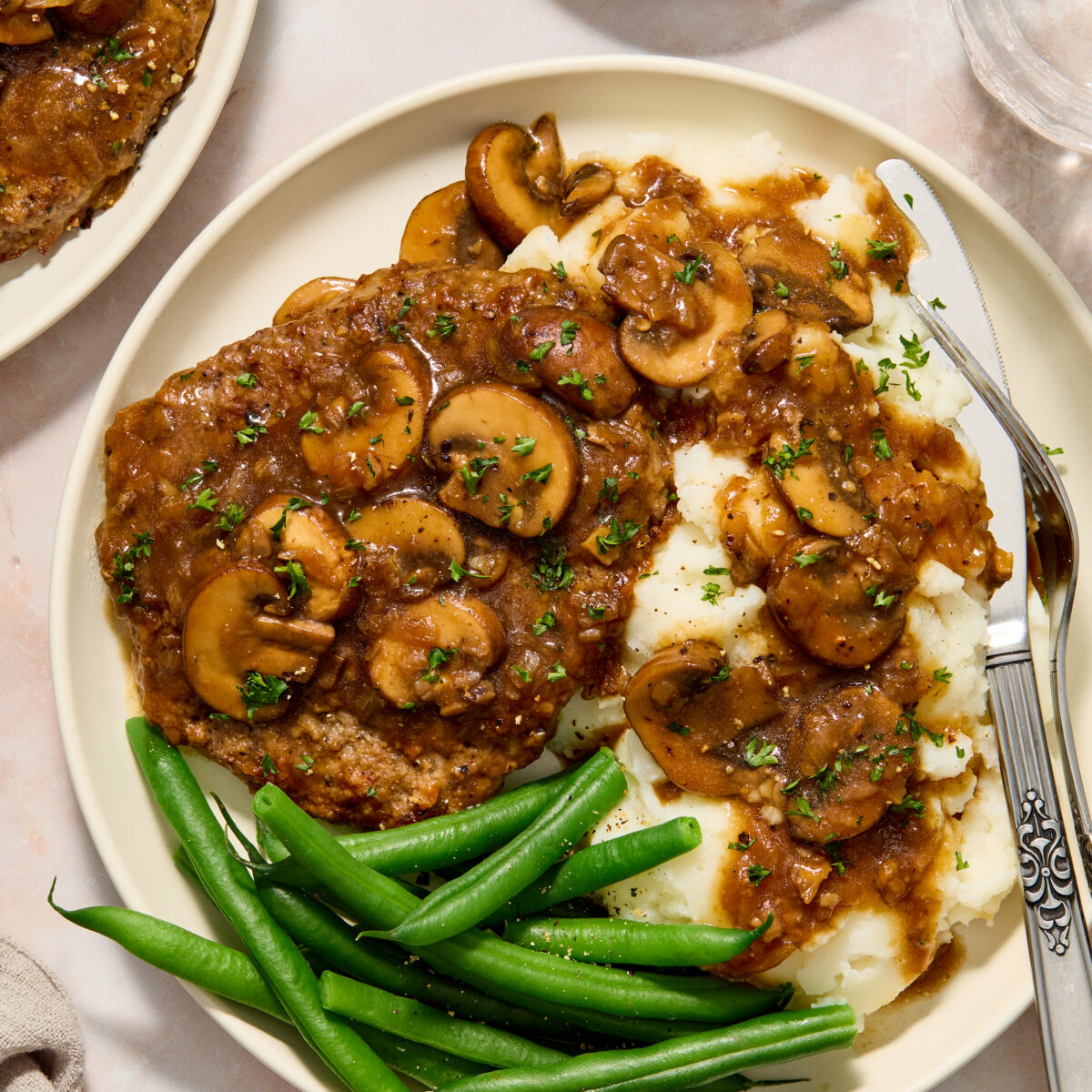 cube steak on a white plate with mashed potatoes and green beans