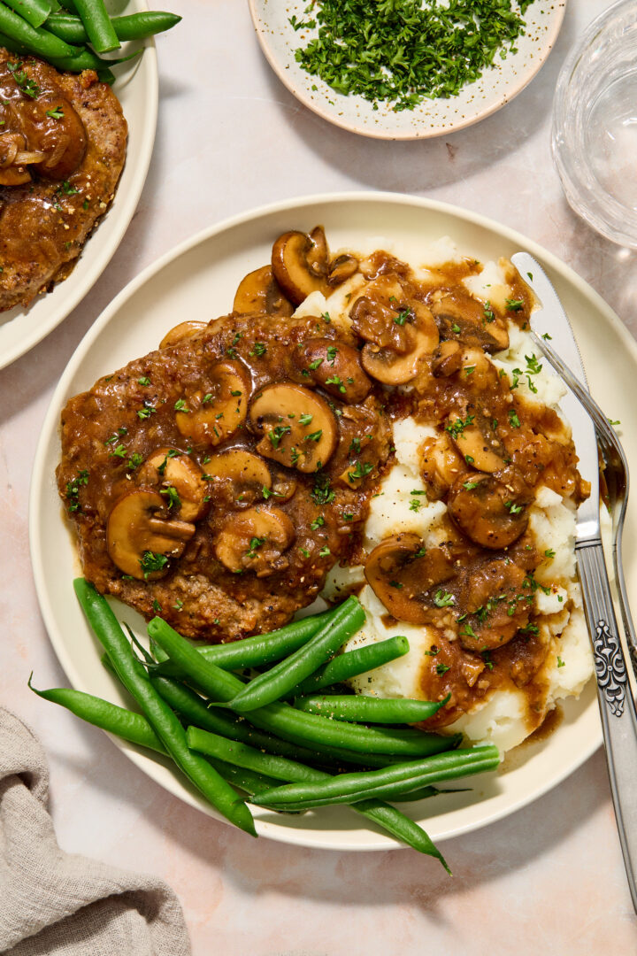 cube steak on a white plate with mashed potatoes and green beans